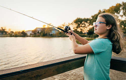 elementary-aged child in glasses fishes off lake dock