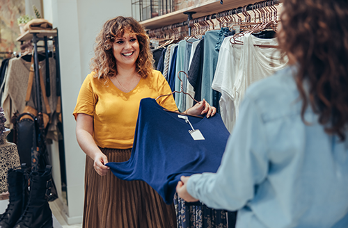 Two shoppers hold up blue top in clothing store
