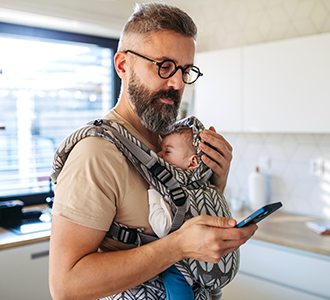 Parent checks smartphone while carrying an infant in a front baby carrier