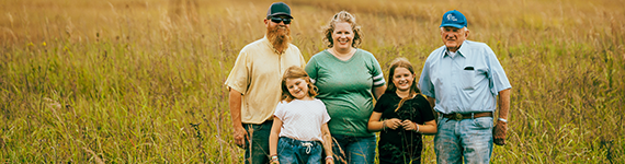 Grandfather, mom, dad and two daughters stand proudly in a field on farm