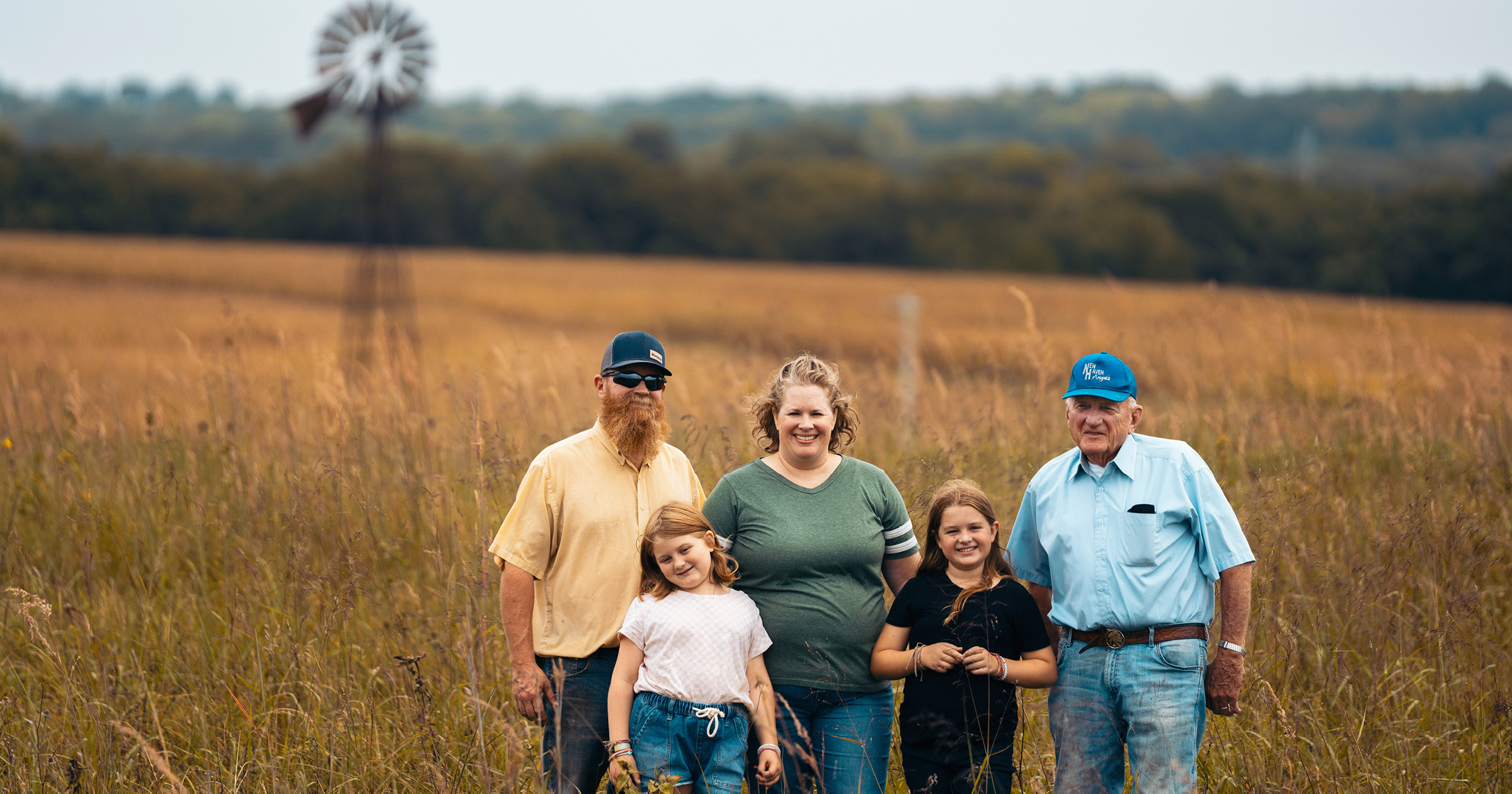 Grandfather, mom, dad and two daughters stand proudly in a field on farm
