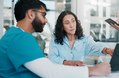 Two medical professionals collaborate around laptop
