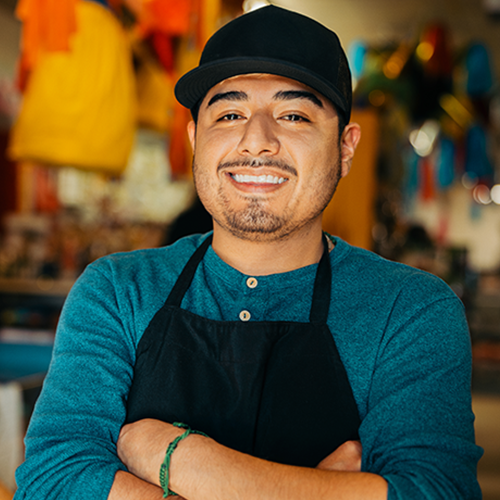 Young business owner smiles proudly while standing in their shop