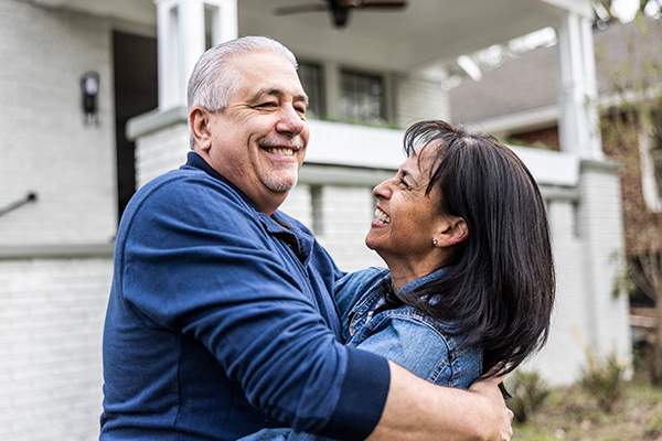 smiling middle-aged couple hugs in front of home