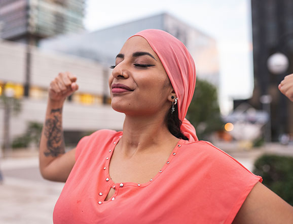 Smiling woman in pink headscarf and shirt flexes muscles in triumph