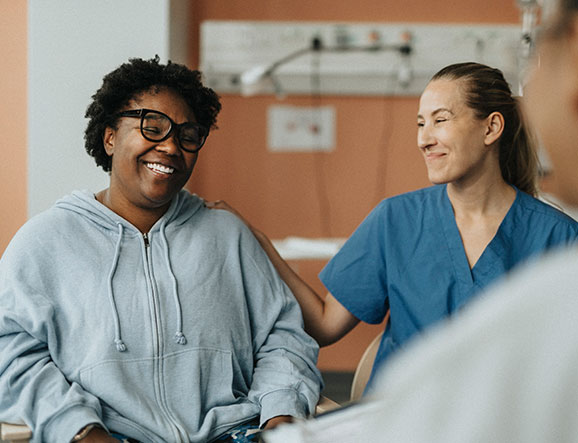 Nurse compassionately puts arm on shoulder of smiling patient in clinical setting