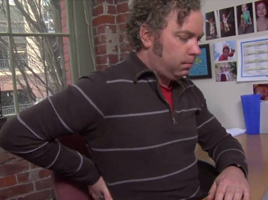 Man sitting at desk holding his back in discomfort