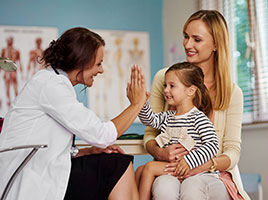 A mother holding her daughter on her lap who is giving the doctor a high five