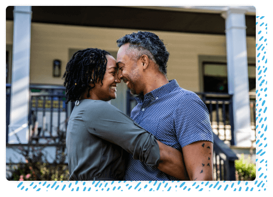 smiling couple hugs in front of house porch