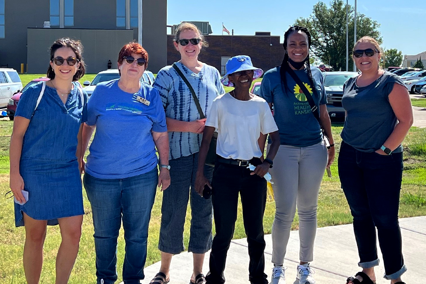 Six smiling people pose together on sidewalk