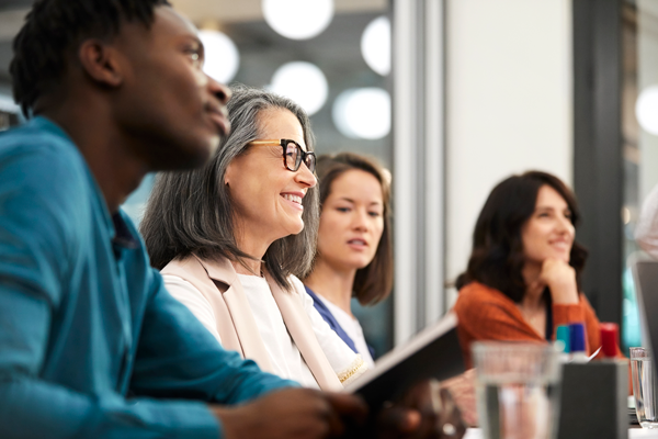 Person with grey hair and glasses smiles during group discussion