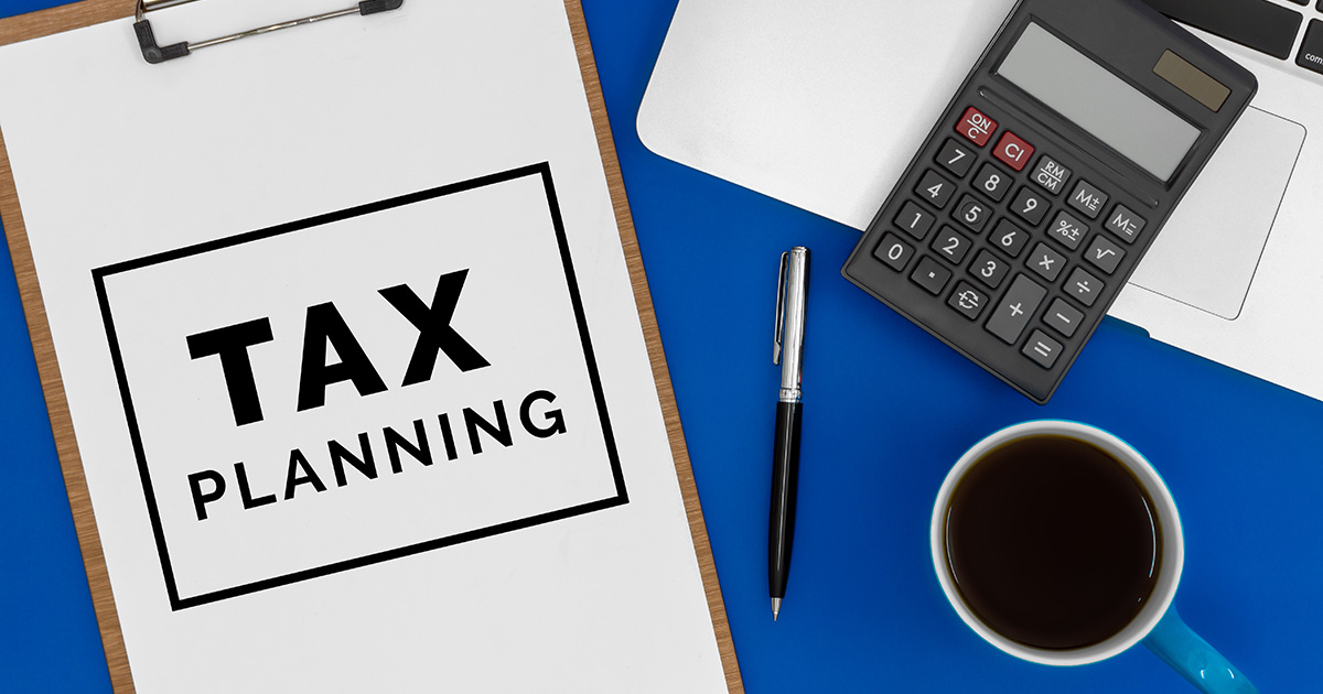 a clipboard with a paper that says TAX PLANNING, pen, calculator, and coffee mug on a desk