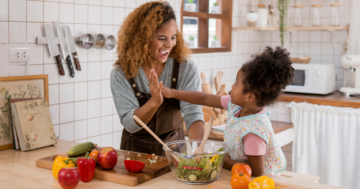 Mother and daughter share a high-five while making a salad