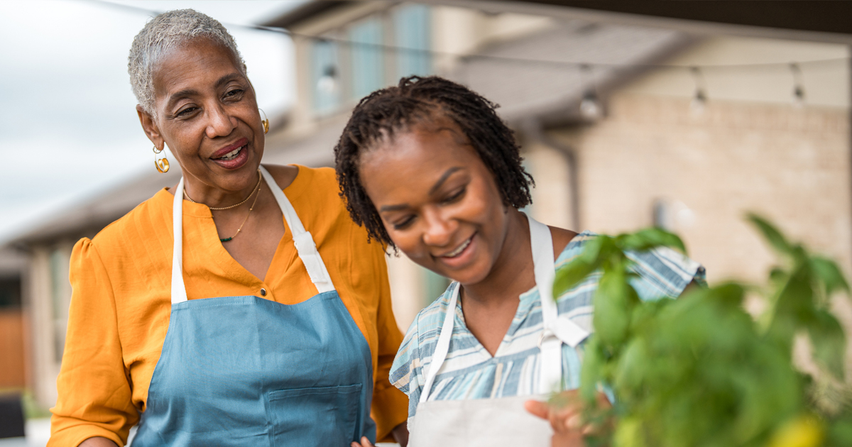 Two people in aprons working together near a garden planter.