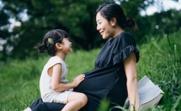 Adult sitting on a blanket in a grassy field with a child seated nearby, outdoors in a park-like setting.