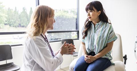 Person seated on an exam table speaking with a healthcare provider in a medical office.